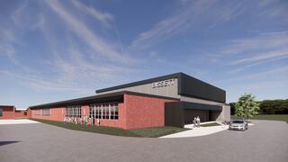 A modern architectural design featuring a brick facade, large windows, and a sleek roof, surrounded by green landscaping and a parking area.