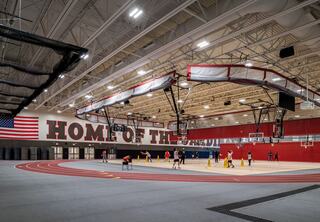A spacious indoor gym features basketball courts, a running track, and an American flag, with people engaging in various activities.