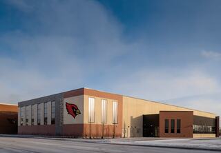 A modern building featuring a cardinal logo, with large windows and a mix of brick and metal finishes, under a clear blue sky.