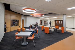 A modern, brightly lit space features casual seating areas with tables, chairs, and vibrant decor, fostering collaboration and interaction.