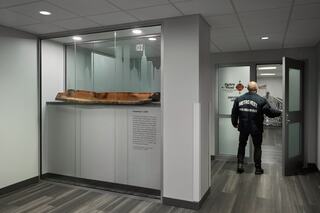 An exhibition space features a display case with an artifact, while a person in uniform stands near the entrance of a room.