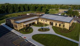 A modern, single-story building surrounded by landscaped greenery, featuring a spacious parking area and a welcoming entryway.