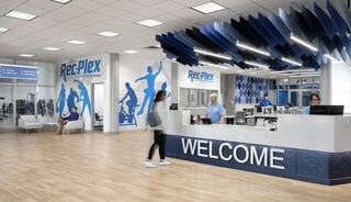 A modern recreational facility features a welcoming reception area with blue accents, fitness graphics on the walls, and staff assisting visitors.