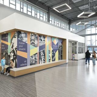 A modern interior featuring vibrant wall graphics with motivational themes, two children sitting, and people moving through a bright, open space.