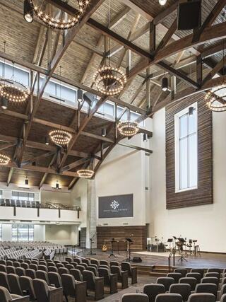 A spacious auditorium featuring wooden beams, elegant chandeliers, and rows of seating, set up for performances or gatherings.