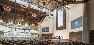 A spacious, modern auditorium featuring high wooden beams, elegant lighting, and rows of seating, designed for gatherings and events.