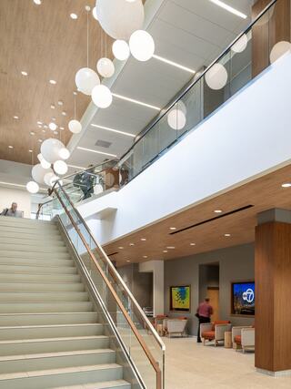 A modern lobby features sleek stairs, contemporary seating, and stylish hanging lights, creating an inviting and airy atmosphere.