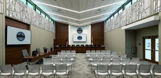 A modern conference room features rows of chairs, a presentation area with screens, and a large emblem on the back wall.
