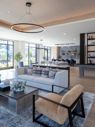 A modern, stylish lounge features a cozy sofa, chic armchair, and large windows, creating a bright and inviting atmosphere.