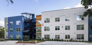 A modern, two-tone residential building features blue and white façades, large windows, and a metal stairway leading to the upper level.