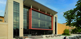 A modern building features large glass panels and a striking red accent. Outdoor seating areas provide a welcoming space.