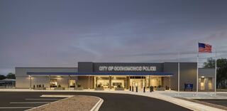 A modern police station features a sleek design, clear signage, and flags, set against a serene twilight sky.