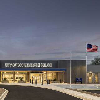 A modern police station features a blue trim, large glass windows, and the flag of the United States, set against a twilight sky.