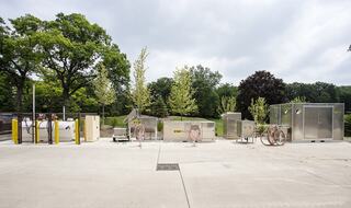 A concrete area features several industrial storage units and equipment, surrounded by trees and greenery.