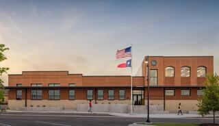 A modern brick building with an entrance featuring steps, flags, and landscaped areas, designed as a police station in a suburban setting.