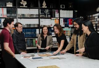 A diverse group of six people collaborates around a table filled with material samples, discussing ideas in a well-organized workspace.