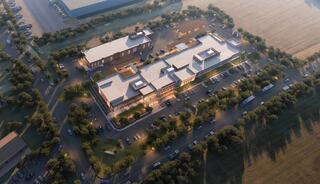 Aerial view of a modern building complex surrounded by trees and parking areas, blending into an open landscape.