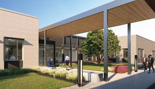 A modern building entrance with large windows, a covered walkway, lush greenery, and people engaged in conversation and walking.