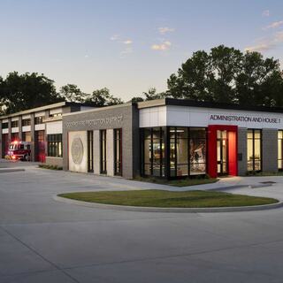 A modern building combining administration and fire protection services, featuring large glass windows and a red accent, set amidst greenery.