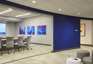 A modern office space features a glass conference room with sleek chairs, colorful wall art, and a bright blue accent wall.