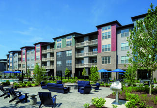 Modern apartment complex with vibrant facade, landscaped gardens, outdoor seating areas, and a pool. Ideal for community living.