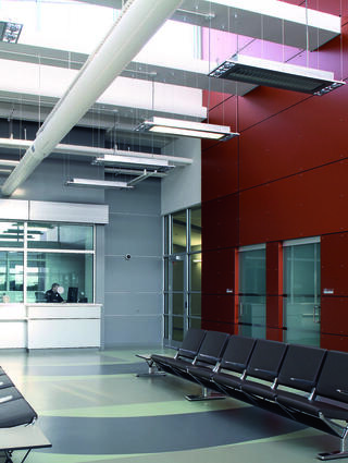 A modern waiting area features sleek benches, a reception desk, and bright walls with a mix of red and gray, creating a clean, spacious environment.