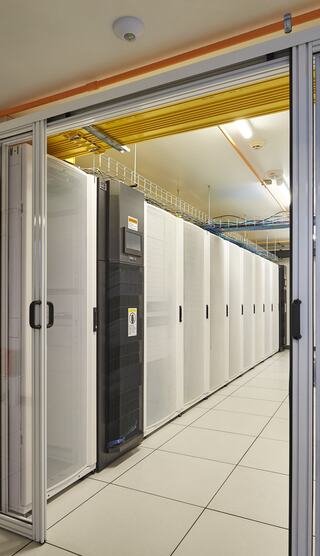 A corridor lined with server racks, featuring a mix of black and white cabinets, illuminated by overhead lights in a data center.