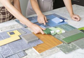Two people review various colored samples and materials, including wood, stone, and fabrics, on a tabletop for a design project.
