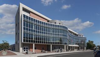 A modern, multi-story building features sleek glass facades and curved architecture, set against a clear blue sky.