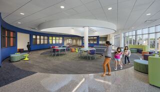A bright, modern space featuring colorful seating, small tables, and children engaged in activities, promoting a collaborative learning environment.