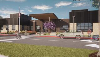 A modern building features large windows, a welcoming entrance, and landscaped areas with pedestrians and vehicles around it.