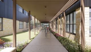 A wide, modern corridor bordered by stone walls and large windows, with lush greenery and colorful flowers on both sides.