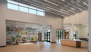 A spacious, modern lobby featuring a colorful mural, sleek furniture, and large windows allowing natural light to flood the area.