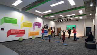 A colorful room with playful wall quotes has children and adults actively participating in an engaging activity, promoting joy and interaction.