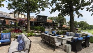 A cozy outdoor seating area with comfortable furniture, surrounded by lush greenery and a picturesque clubhouse in the background.