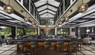 A spacious, elegantly designed dining area with a long bar, stylish seating, and large windows showcasing lush outdoor views.