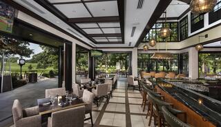 A stylish restaurant features modern decor, elegant furnishings, and large windows overlooking a scenic outdoor space, creating a vibrant atmosphere.