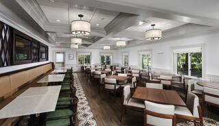 A spacious dining area features wooden tables and chairs, elegant lighting, and large windows allowing natural light to illuminate the room.