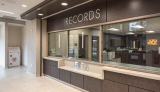 A modern office space features a reception area labeled "RECORDS," with a service window and a clean, professional design.