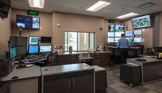 A modern control room with multiple screens displays data and surveillance, while an operator monitors activities at a workstation.