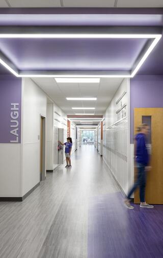 A modern school hallway features bright lighting, sleek floors, and a motivational word "LAUGH" on the wall, with students walking by.