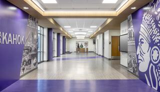 A modern hallway features purple walls with historical images and text, leading to a bright, open space with doors and windows.
