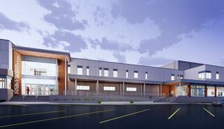 A modern school building features large windows, a welcoming entrance, and a sleek design, set against a cloudy evening sky.