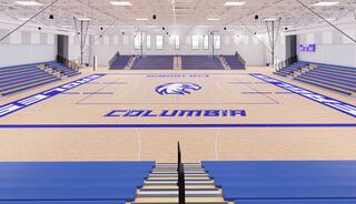 A spacious gymnasium features blue bleachers and a wooden court marked with "Columbia" and an eagle logo, bathed in natural light.
