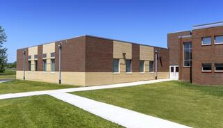 A single-story brick building features a mix of light and dark tones, surrounded by green grass and a pathway under a clear blue sky.