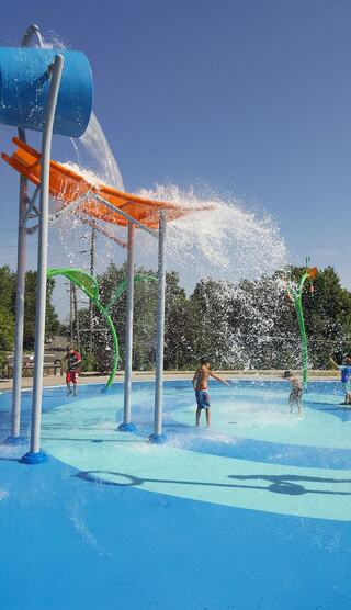 Children play joyfully in a vibrant water splash park, featuring colorful slides and sprays under a clear blue sky.