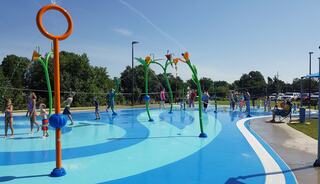 A vibrant splash pad with colorful water features and children playing in the sun, enjoying a refreshing day of fun and laughter.