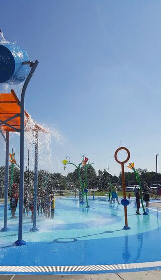A vibrant splash pad with colorful water features and children joyfully playing under bright sunshine.