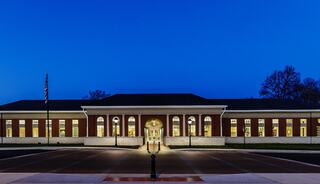 A well-lit, modern brick building stands against a deep blue twilight sky, featuring an inviting entrance and wide windows.