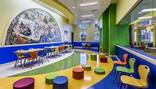 A colorful room features bright chairs and tables, with a large mural on the wall, creating an inviting space for children.